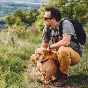 Image of a man and his dog hiking on a grassy hill